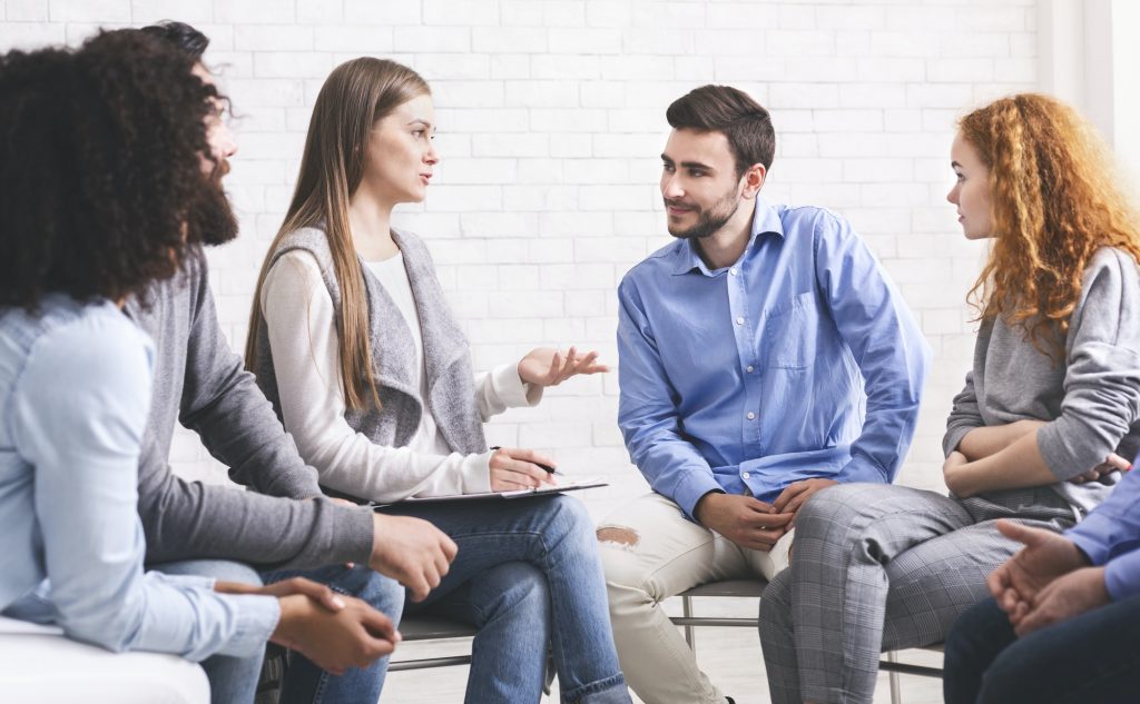 People sitting in circle and listening mentor during group therapy session