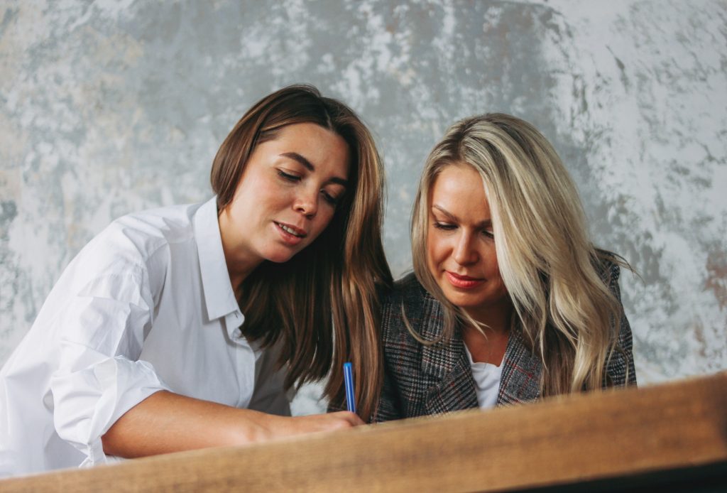Young successful women colleagues discuss joint project, coaching at table